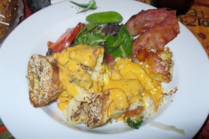 Savory bread pudding with cheese sauce, mixed green salad, and a slice of crispy bacon.